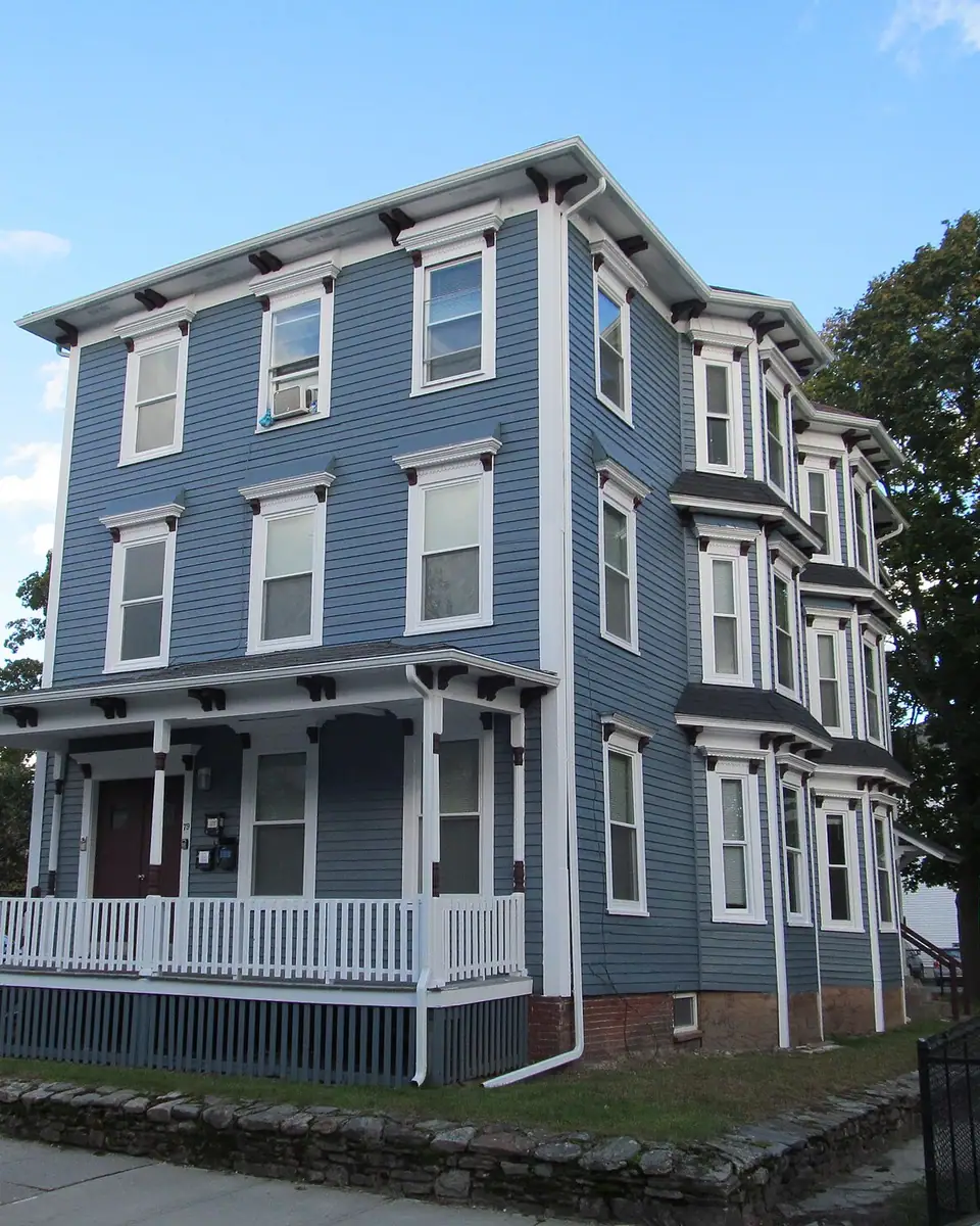 A blue Worcester three-decker with a wide front porch, bracketed eaves and bay windows stacked three floors high